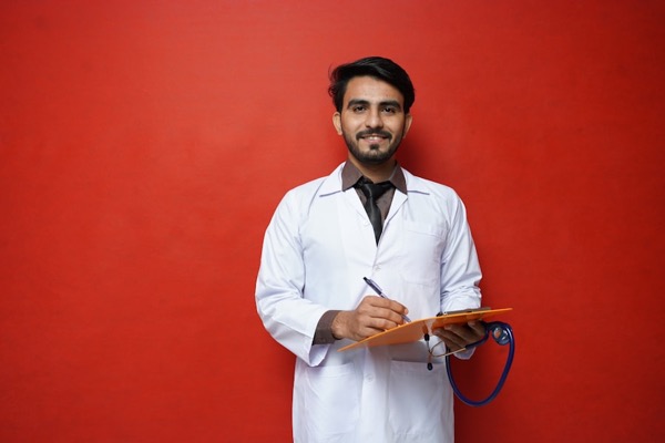 a scientist holds a clipboard against a red wall, looking concerned